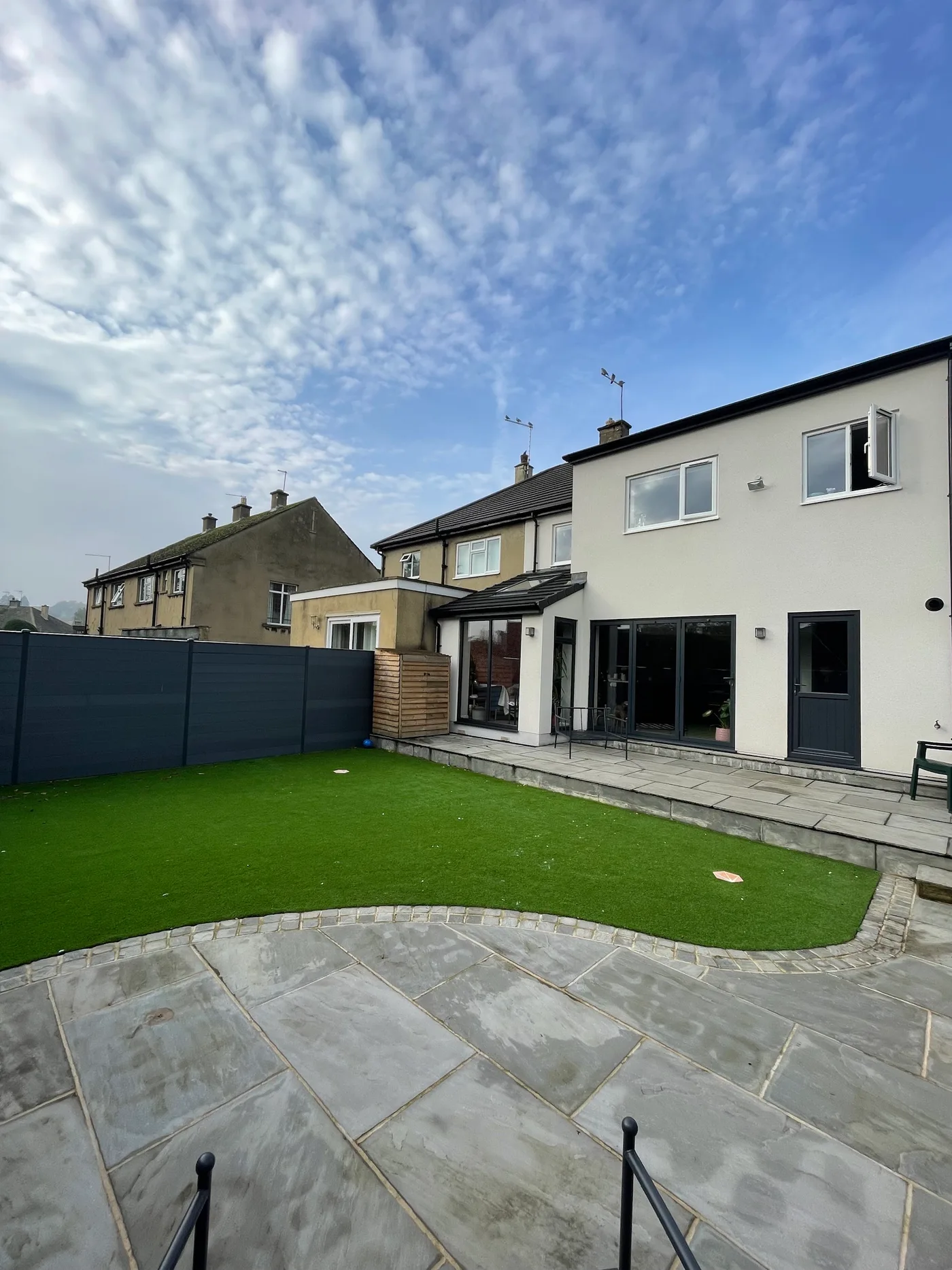Artificial lawn edged by a curved stone patio and composite fence