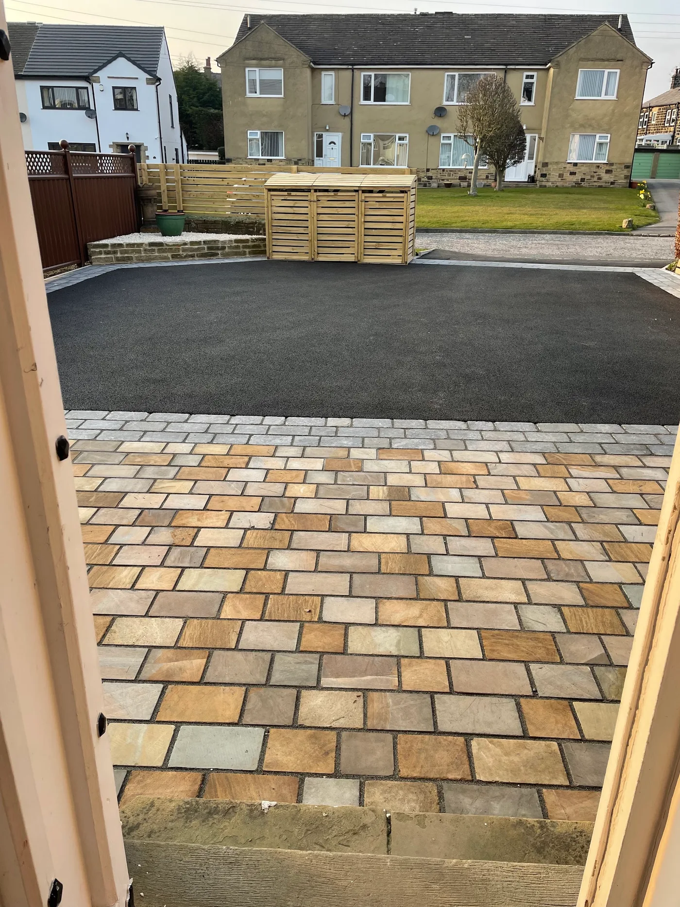 Stone paving and tarmac driveway with a timber bin store